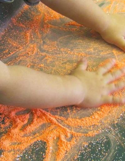 Oakwood Community Pre-school | Gallery | Child spreading coloured sand around